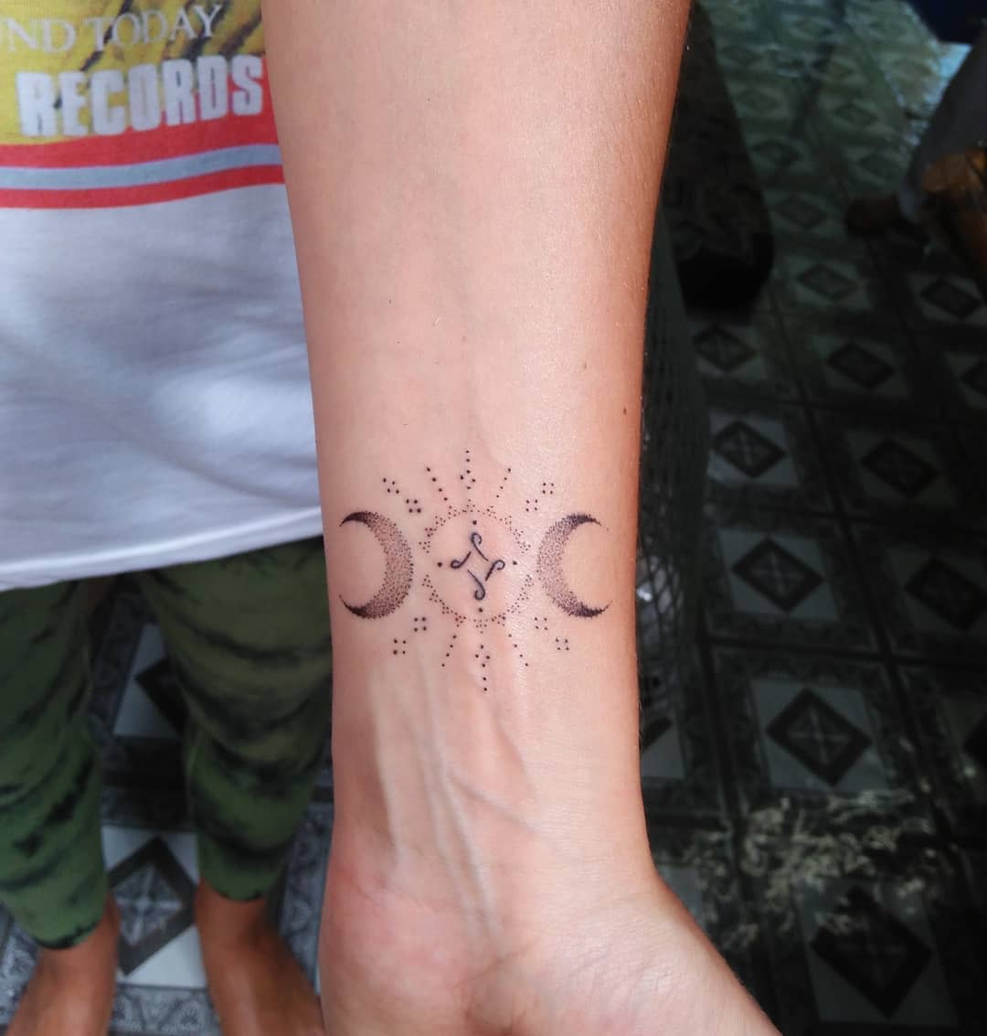Forearm tattoo with crescent moons, starburst, and dots design